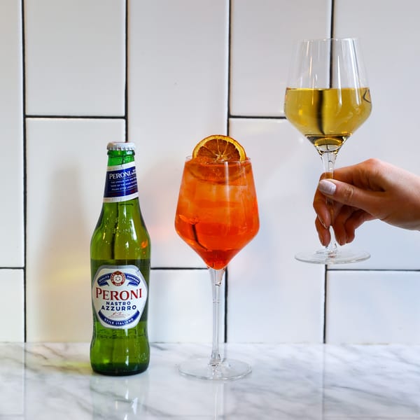 A Peroni beer bottle, an Aperol Spritz, and a glass of white wine on a marble surface.