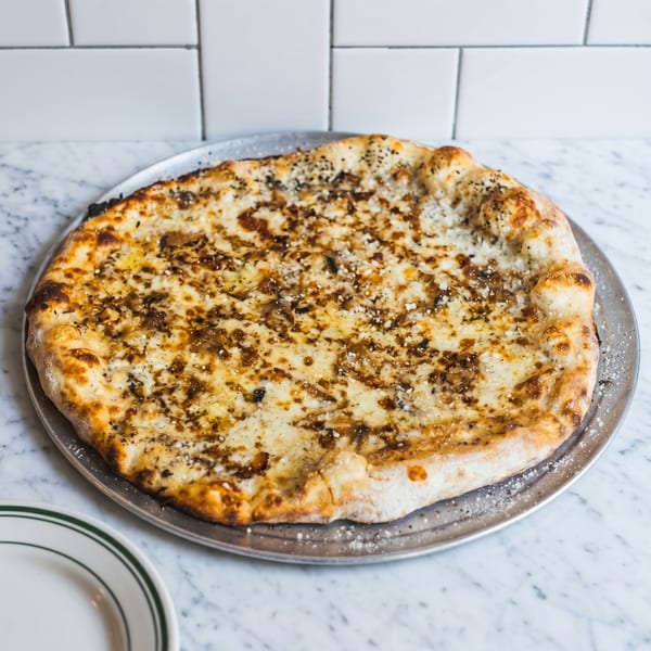 A whole white pizza with caramelized onions and cheese on a metal pan.
